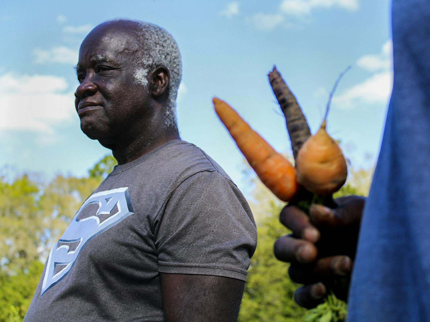 Lennon Fisher Jr. holds three different kinds of carrots in his hand while Lennon Fisher looks at the field. They said some of their favorite produce are their carrots.