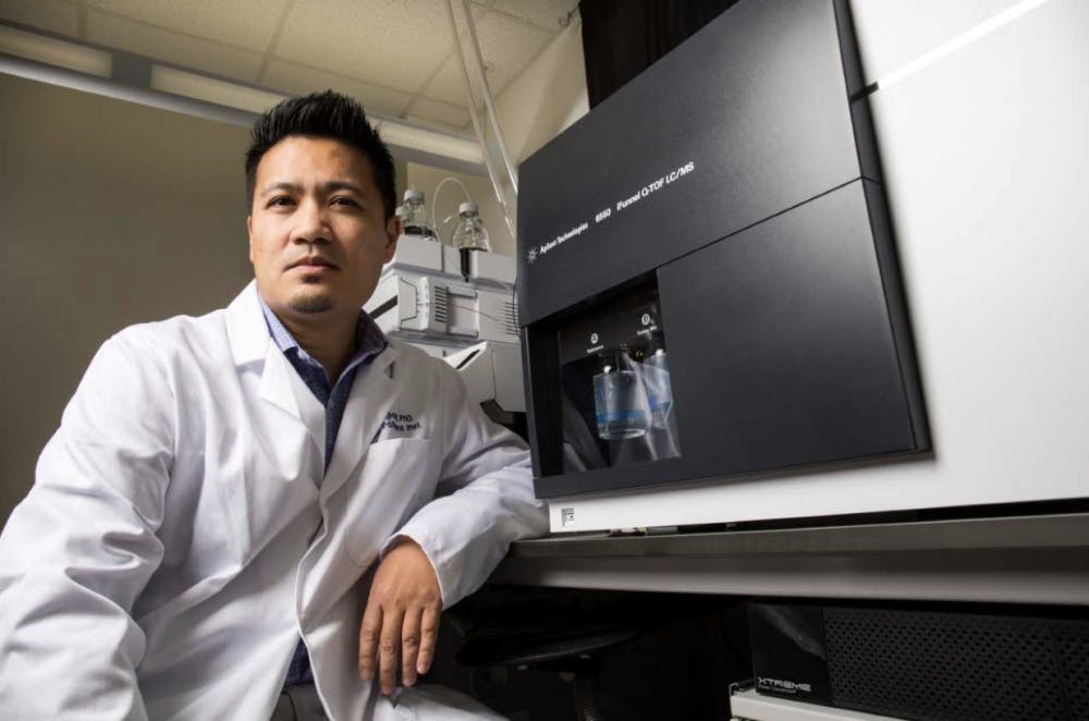 Rhoel Dinglasan, UF associate professor of infectious diseases and leader of the project which developed the Saliva-based Malaria Asymptomatic Asexual Rapid Test device, sits next to one of his agilent mass spectrometers which was used to gather data. Courtesy to The Alligator.