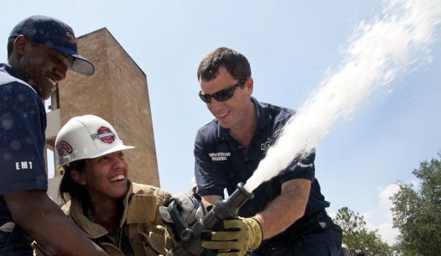CITIZENS' FIRE ACADEMY -- Reggie Kinsey, 24, an EMT at Station 7, and Greg Fenn, 32, a driver/operator at Station 1, assist Mary Ann Dematas, 30, with a 1 1/4 inch (diameter) fire hose, spraying 170 gallons of water per minute, Saturday at Station 3, near Waldo Road and 8th Avenue. Dematas, who works in the Lawn and Gardening Department at Home Depot, tried to compare the water pressure to a difficult task, but carrying 30-pound bags of soil doesn't illustrate the constant force her body stood against.
