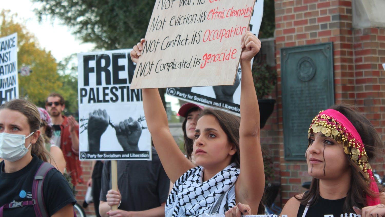 A attendee at the &quot;Stand with Palestine&quot; protest holds a &quot;Not war, it&#x27;s colonialism; not eviction, it&#x27;s ethnic cleansing; not conflict, it&#x27;s occupation; not complicated, it&#x27;s genocide&quot; sign at the corner of University Avenue on Monday, Oct. 23, 2023. 