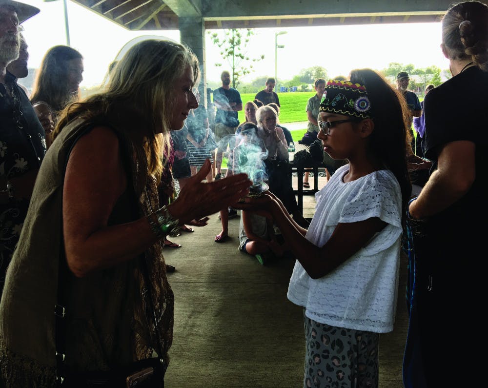 <p dir="ltr">Lily Smith, 11, welcomed guests at a Wednesday night water ceremony held at Depot Park, located at 200 SE Depot Ave., by smudging them with sage. At the ceremony, about 30 people sang, danced and discussed the importance of the four elements — especially water.</p>