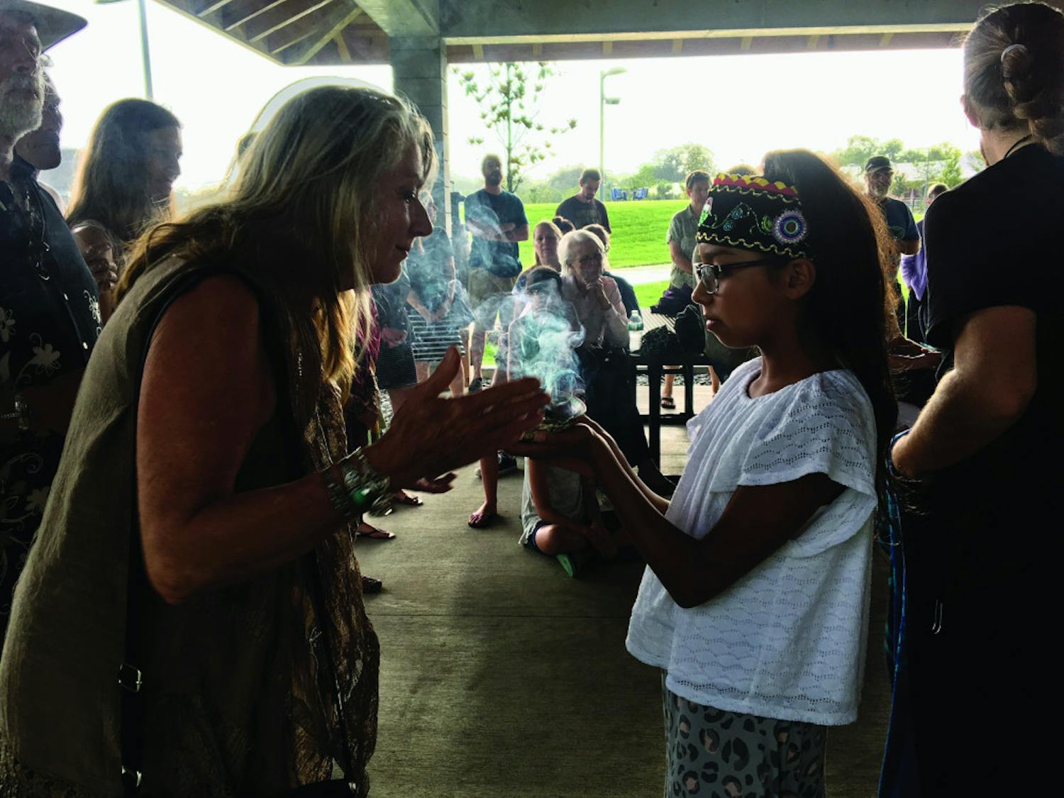 Lily Smith, 11, welcomed guests at a Wednesday night water ceremony held at Depot Park, located at 200 SE Depot Ave., by smudging them with sage. At the ceremony, about 30 people sang, danced and discussed the importance of the four elements — especially water.