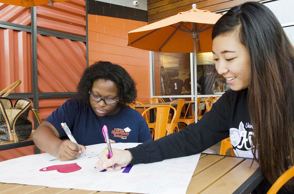 Kendra Phillip (left), 22-year-old UF health education graduate, and Athena Wong, 19-year-old UF accounting sophomore, sign a giant card for Roselle Derequito at Blaze Wednesday. Derequito's sorority, alpha Kappa Delta Phi, held a fundraiser to raise money for her medical expenses.