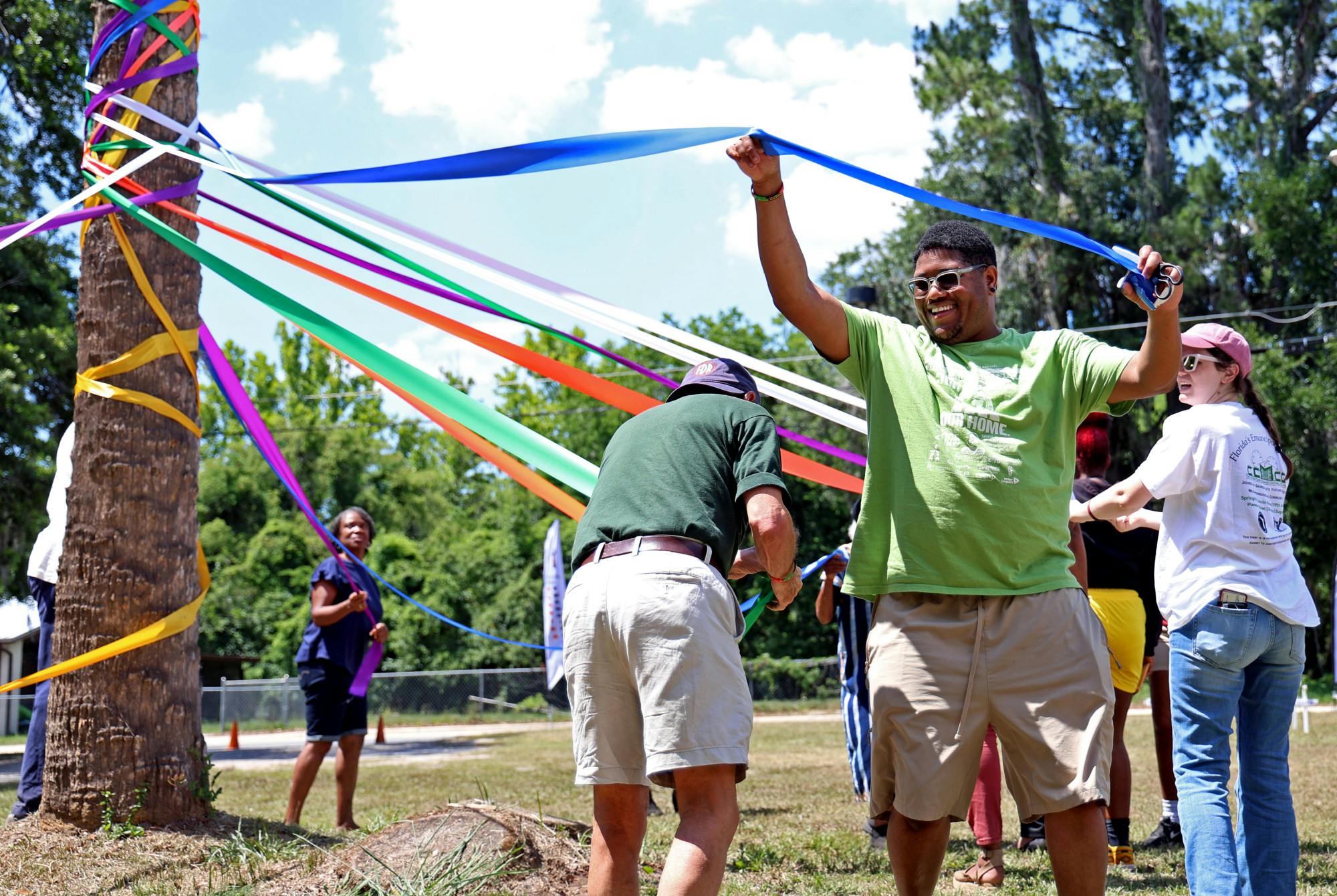 Errol Nelson weaves a blue ribbon around a palm tree maypole alongside 11 others during the Florida Emancipation Celebration at the Cotton Club Museum and Cultural Center in Gainesville, on May 24, 2025. Each year, attendees join together to plait the maypole in honor of Florida’s Emancipation Day, which occurred on May 20, 1865.