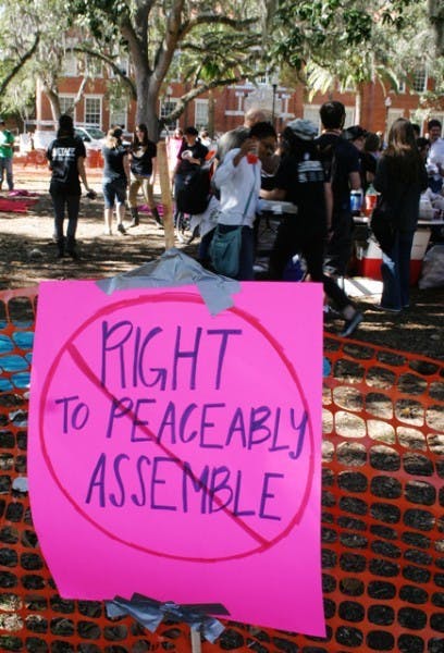 A sign reading "Right To Peaceably Assemble" with a cross through it is posted at the First Amendment Free Food Festival on the Plaza of the Americas Wednesday afternoon.