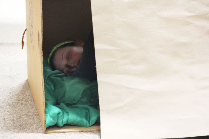 High school senior Alex Martin gets ready to fall asleep in a makeshift shelter she made out of cardboard at F. W. Buchholz High School on Saturday evening. Students spent the night sleeping outside on the cafeteria patio floor as part of a homelessness awareness event.