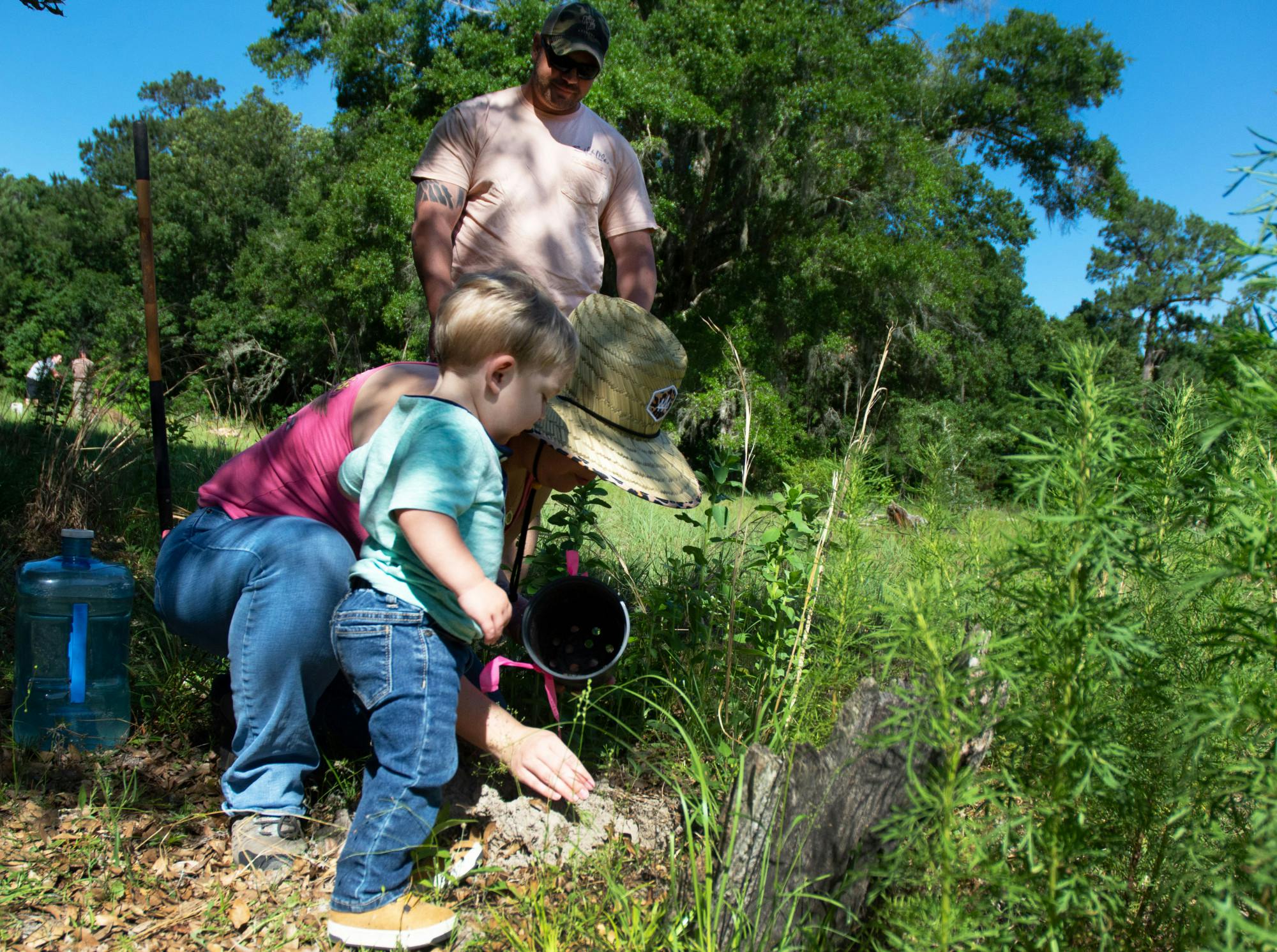 Jillian Rexroat and son, Jaxson Rexroat, (left) arrange dirt as Matt Rexroat (right) smiles at the two of them at his grandmother-in-law’s grave in the Prairie Creek Conservation Cemetery on Saturday, May 15, 2021. The family was there for Community Planting Day in the meadow area of the cemetery. 
