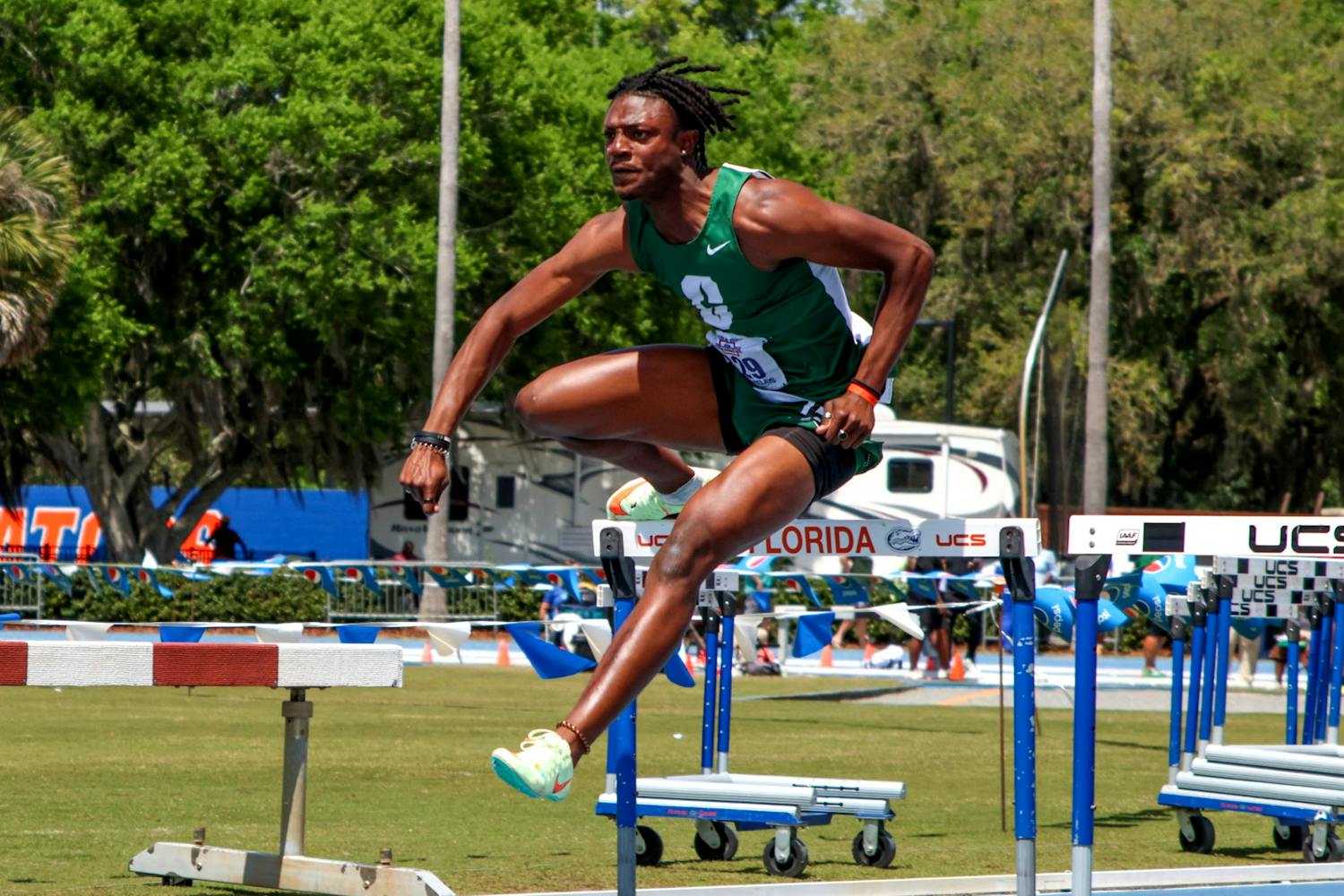 UNC Charlotte track and field athlete Sam Thompson clears a hurdle wearing a green uniform similar to his high school attire during the Pepsi Florida Relays Friday, March 31, 2023. Thompson was a student at UF before he transferred and joined UNC Charlotte&#x27;s team.