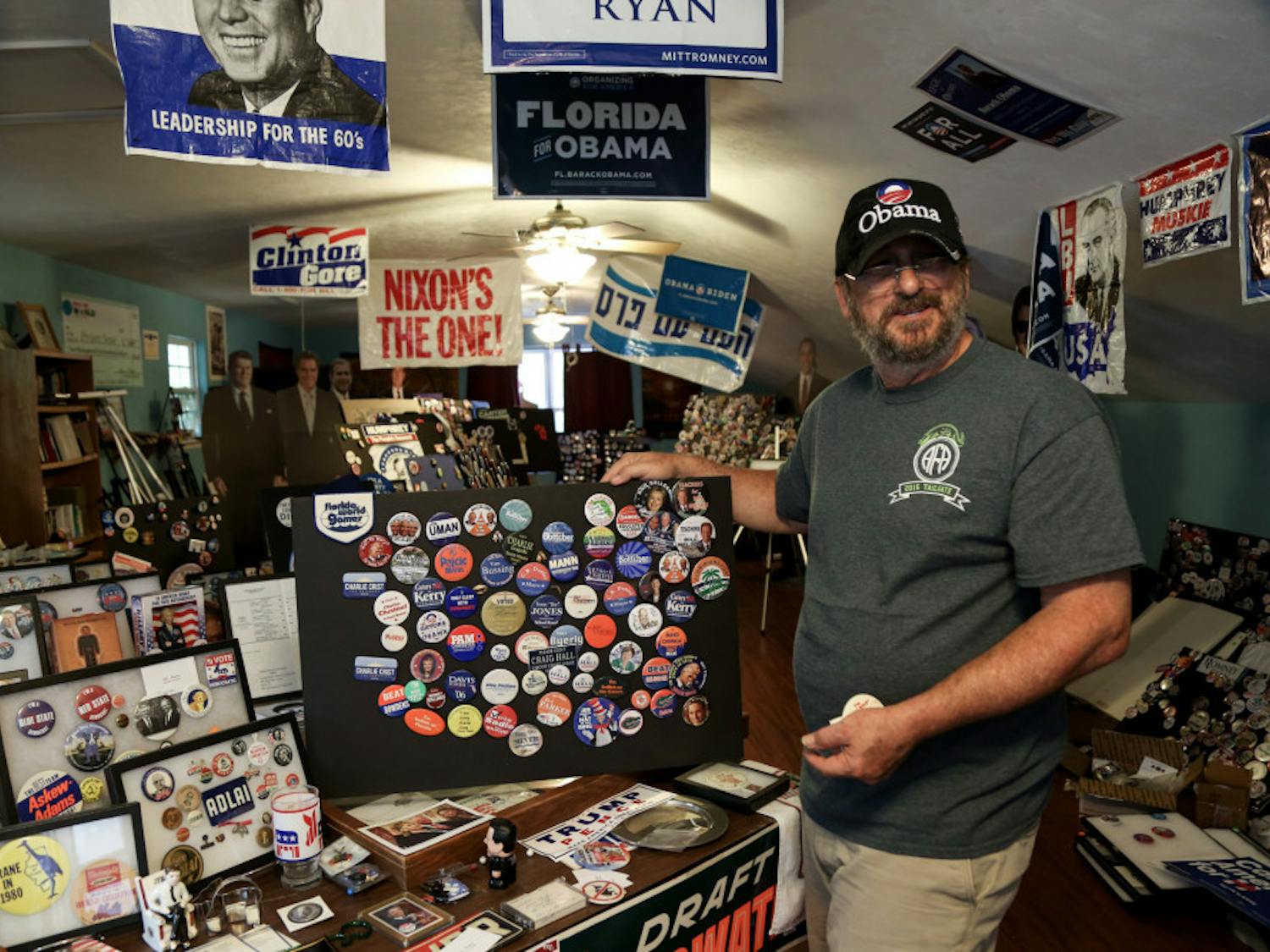 By Melissa Gomez
When Bill Clinton visited Gainesville on Saturday, Ed Kellerman got the former president to sign his favorite shirt.
When the 64-year-old UF master lecturer met Bill Clinton, he handed him a frame full of political buttons, one of which he created.
“I feel privileged he has one of my buttons now,” Kellerman said.
The second floor of the Gainesville resident’s house is decorated in memorabilia, mostly from presidential elections, ranging from buttons and bobbleheads to banners and trinkets. The trinkets, some of which are about a decade old, span the political spectrum, but he considers himself a Democrat.
Kellerman said he remembers when Bill Clinton visited UF in 1992, a scene he captured with a camera and put onto one of the buttons he gave to Bill Clinton on Saturday.
Cardboard cutouts of former presidents sit in his house, along with two lifesize cutouts of Hillary Clinton. He has a blue cone that reads “Holler for Change” and a beer can that reads “Billary Beer.”
On Wednesday, the day after the election, he said he plans on bringing both of the cutouts of Hillary Clinton to one of his classes to show support for her presidency.
Kellerman said Hillary Clinton’s background as secretary of state proves she has the diplomacy skills to succeed as the next president.
“If she’s not ready, then who is?” he said.