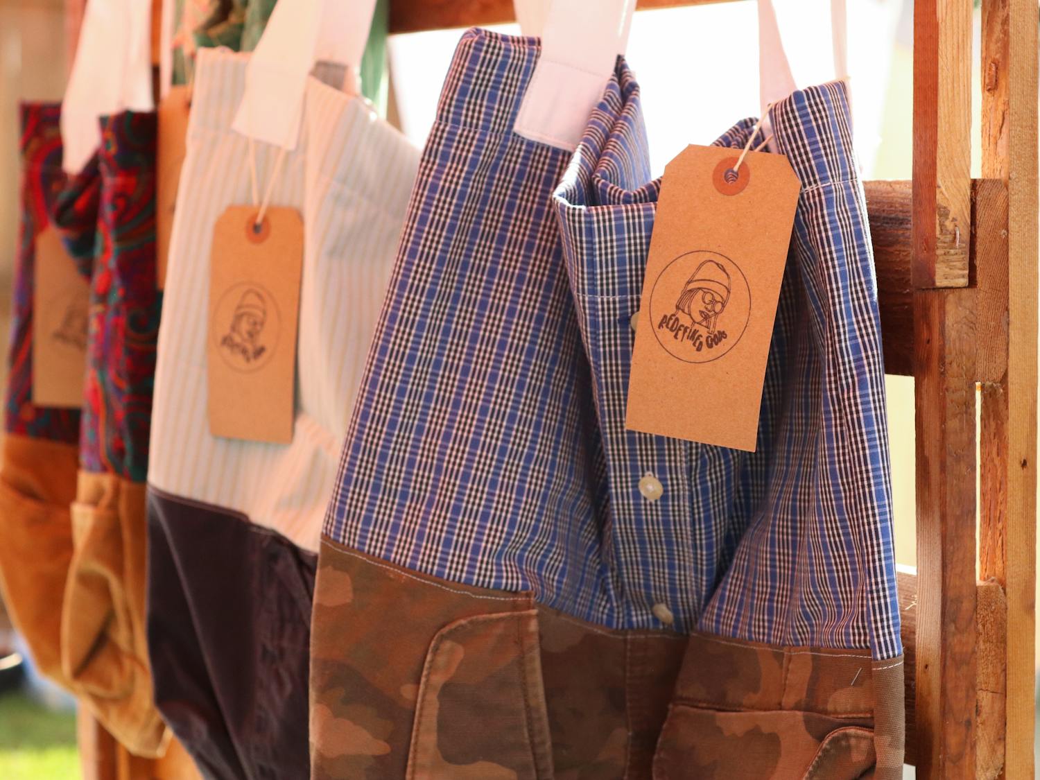 Handmade tote bags hang for sale in Mia Crisostomo's tent at the Gainesville Indie Flea Pop Up market Sunday. The bags, repurposed out of thrifted shirts, are just one of the ways Crisostomo's business promotes sustainable fashion.
