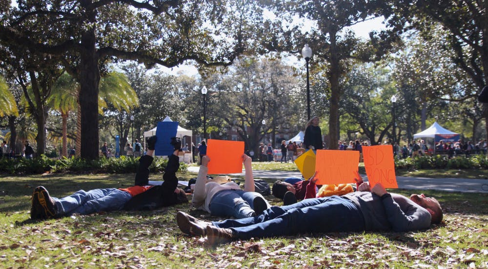 Students lie on the grass at Plaza of the Americas holding signs as a part of Indivisible UF's lie-down protest Wednesday morning.  
