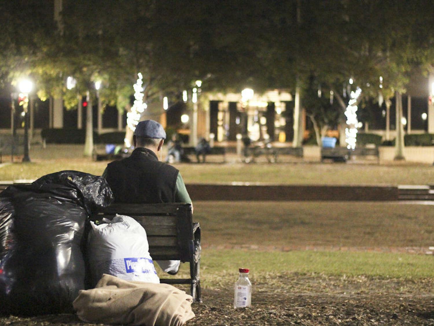 A resident of Bo Diddley Community Plaza sits on a bench on the plaza, looking across at Christmas lights Thursday night. The plaza will close due to renovations, leaving a lot of its residents without a place to stay.