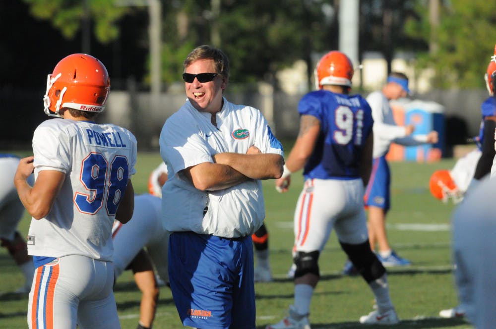 <p>Jim McElwain talks with players during stretches before a fall practice at Donald R. Dizney Stadium. </p>