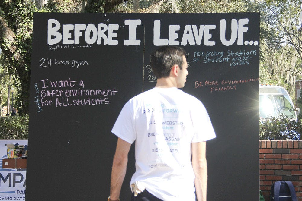 Blake Giragos, a UF graduate student in management and a member of Impact Party, encourages students to write changes they would like to see at UF before they graduate on a blackboard on Turlington Plaza on Tuesday.