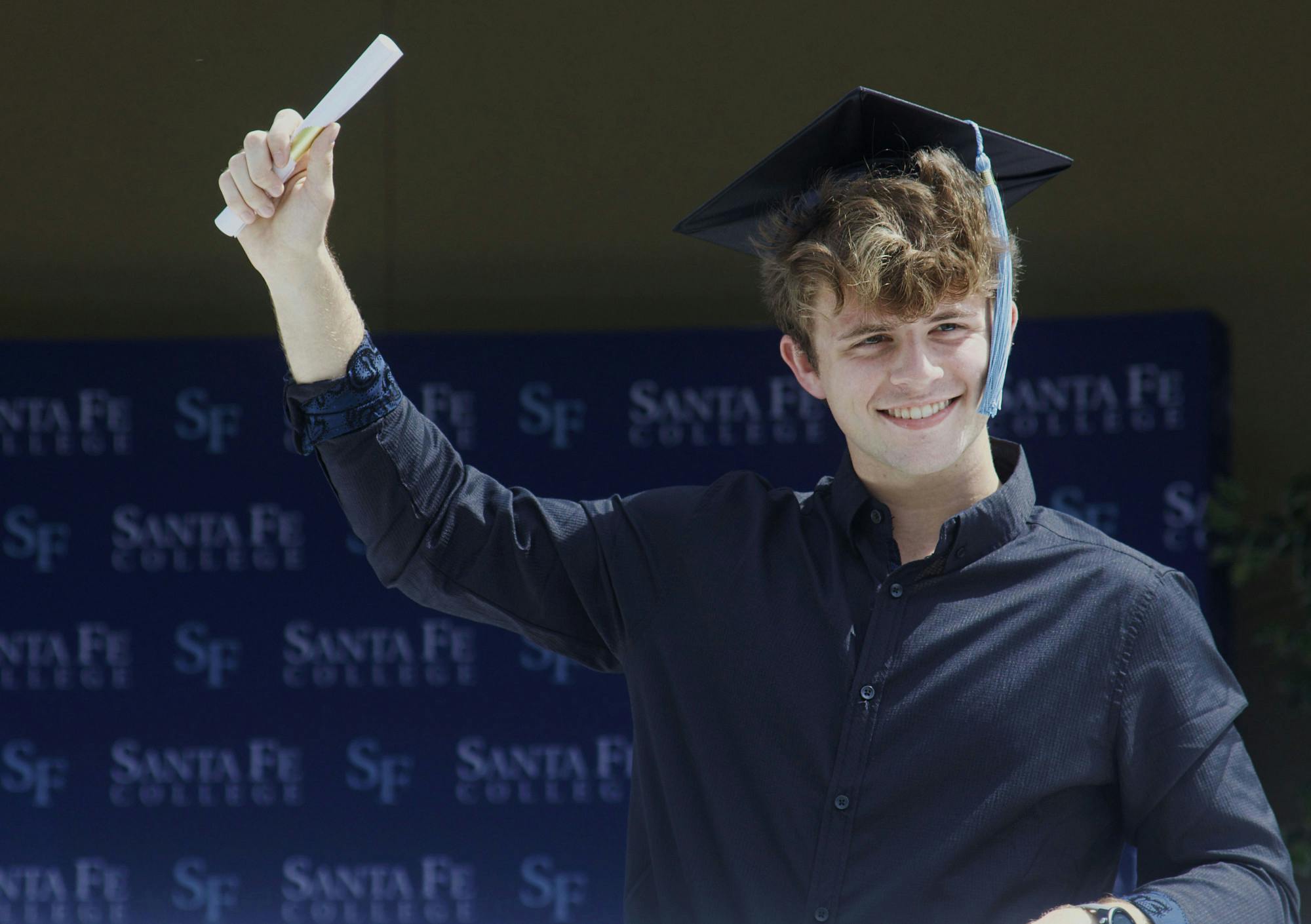 Alexander McCollum, 19, a Santa Fe Associate of Arts graduate stands through the sunroof of a white limousine with his hand holding a paper scroll raised in the air in celebration during Santa Fe College’s Drive-Thru Grad Walk ceremony on Thursday, April 29, 2021.