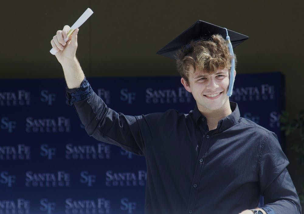 <p>Alexander McCollum, 19, a Santa Fe Associate of Arts graduate stands through the sunroof of a white limousine with his hand holding a paper scroll raised in the air in celebration during Santa Fe College’s Drive-Thru Grad Walk ceremony on Thursday, April 29, 2021.</p>