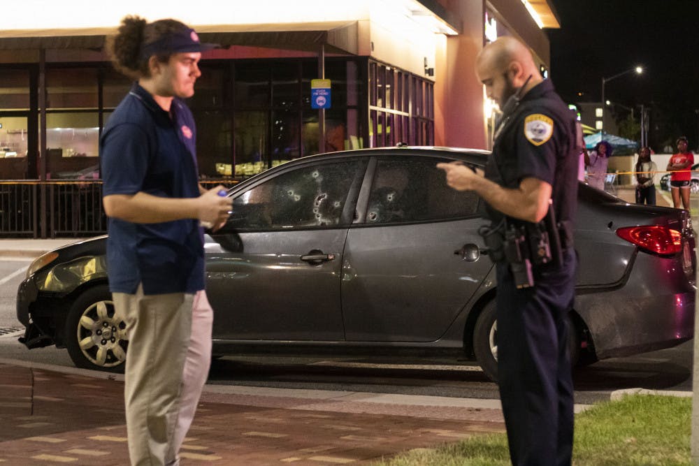 Nico Diaz, 22, talks with an officer Sunday night in front of the Jersey Mike’s in Butler Plaza. Behind them is a gray Hyundai with at least ten bullet holes. 