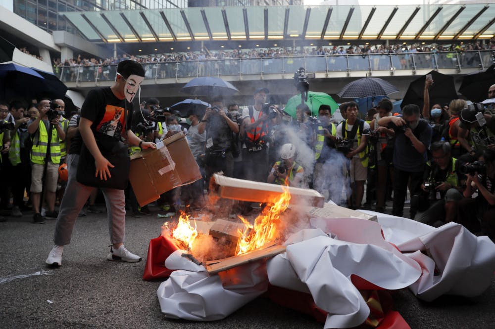 A masked protester sets fire to a China 70th anniversary celebration banner in Hong Kong, Friday, Oct. 4, 2019. Hong Kong Chief Executive Carrie Lam announced that protesters are banned from wearing masks to conceal their identities in a hardening of the government's stance against the 4-month-old demonstrations. (AP Photo/Kin Cheung)