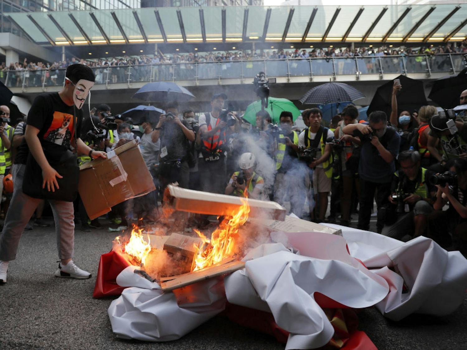 A masked protester sets fire to a China 70th anniversary celebration banner in Hong Kong, Friday, Oct. 4, 2019. Hong Kong Chief Executive Carrie Lam announced that protesters are banned from wearing masks to conceal their identities in a hardening of the government's stance against the 4-month-old demonstrations. (AP Photo/Kin Cheung)