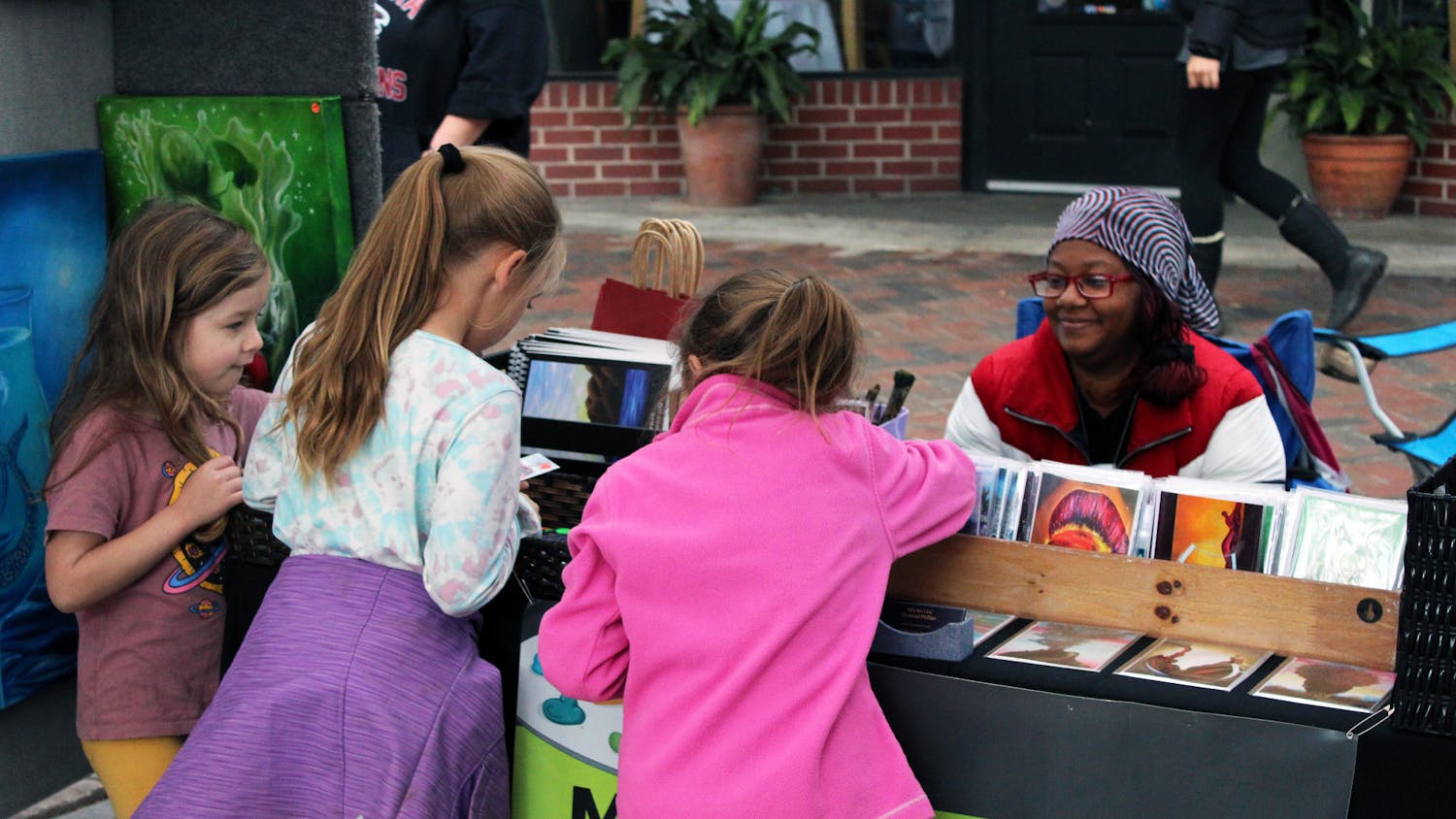 Juliette Walrath (left), 5, Brianna Derrick (middle), 7, and Isabelle Derrick (right), 5, pick their favorite postcards from Atlanta artist Dymond Phillips’ booth at the Gainesville Downtown Festival &amp; Art Show Saturday, Nov. 19, 2022. 
