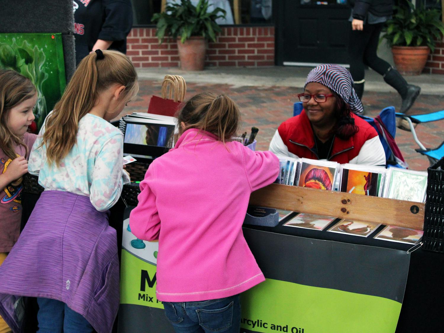 Juliette Walrath (left), 5, Brianna Derrick (middle), 7, and Isabelle Derrick (right), 5, pick their favorite postcards from Atlanta artist Dymond Phillips’ booth at the Gainesville Downtown Festival & Art Show Saturday, Nov. 19, 2022.