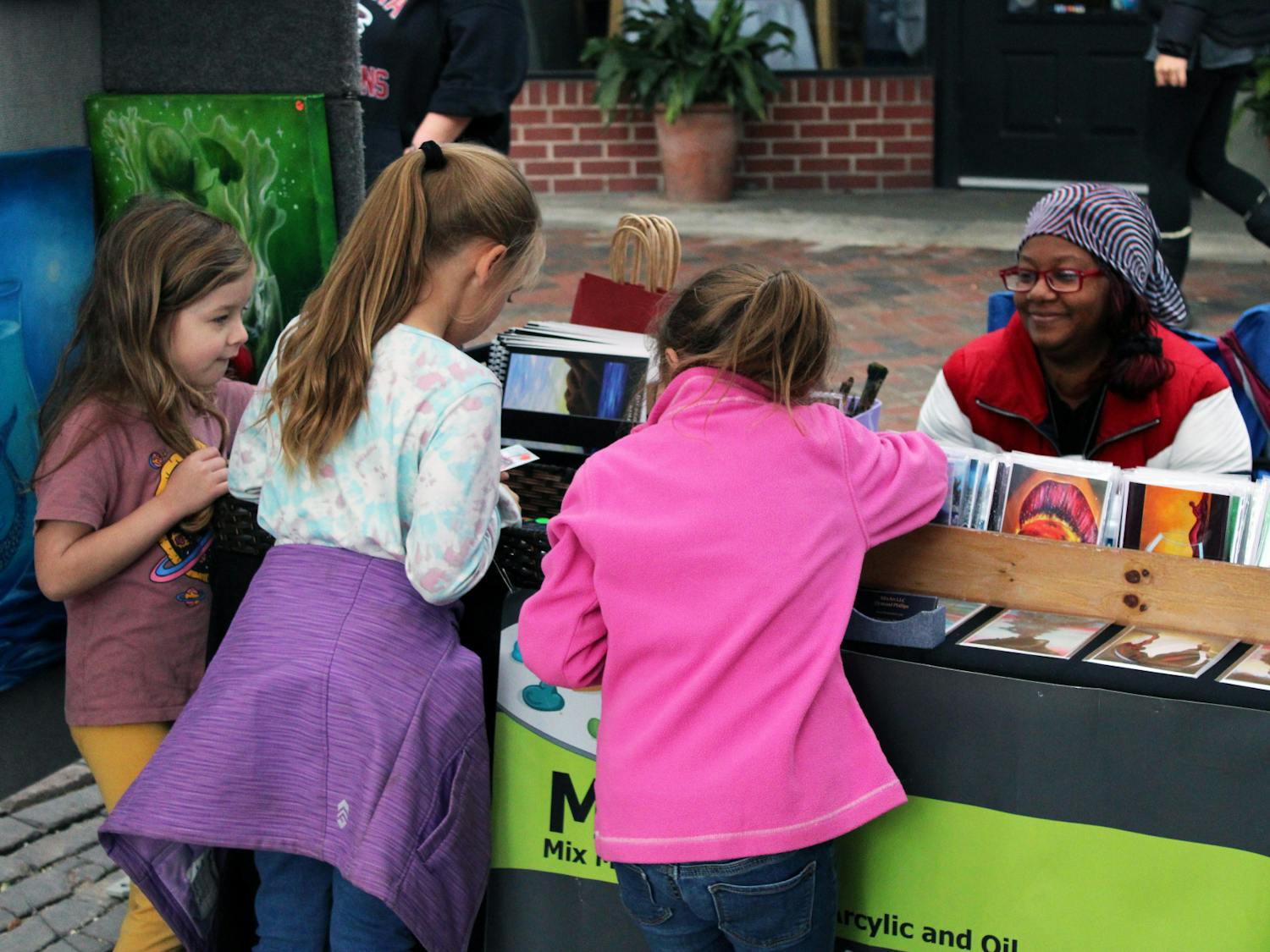 Juliette Walrath (left), 5, Brianna Derrick (middle), 7, and Isabelle Derrick (right), 5, pick their favorite postcards from Atlanta artist Dymond Phillips’ booth at the Gainesville Downtown Festival &amp; Art Show Saturday, Nov. 19, 2022. 