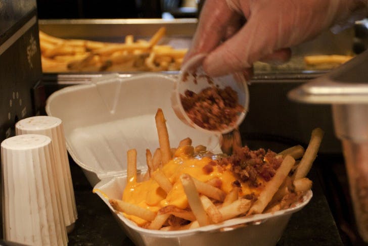 Accounting junior Sam Coccia, 20, dumps bacon bits on an order of loaded french fries Friday afternoon at the Midtown location of Relish. Loaded fries are the closest meal to poutine, which is not yet available.