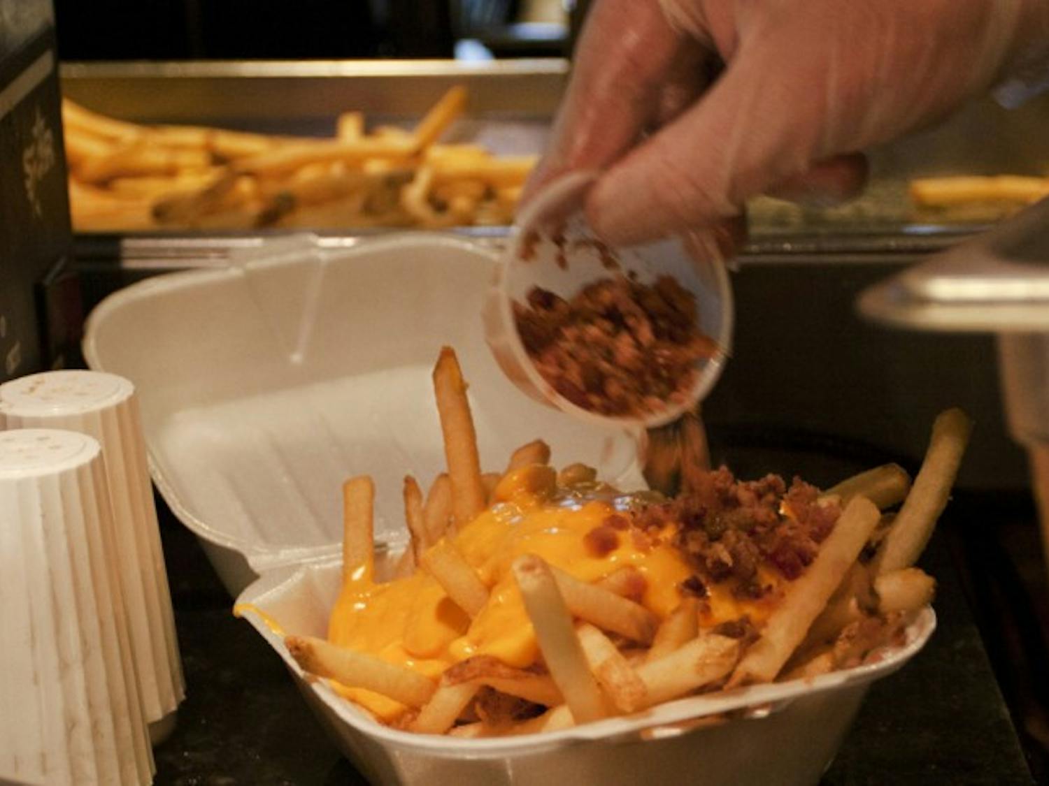 Accounting junior Sam Coccia, 20, dumps bacon bits on an order of loaded french fries Friday afternoon at the Midtown location of Relish. Loaded fries are the closest meal to poutine, which is not yet available.