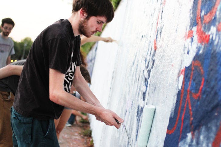 Josh Bush, a 21-year-old UF computer science student, paints on the 34th Street Wall as part of a UF SDS event Monday evening.