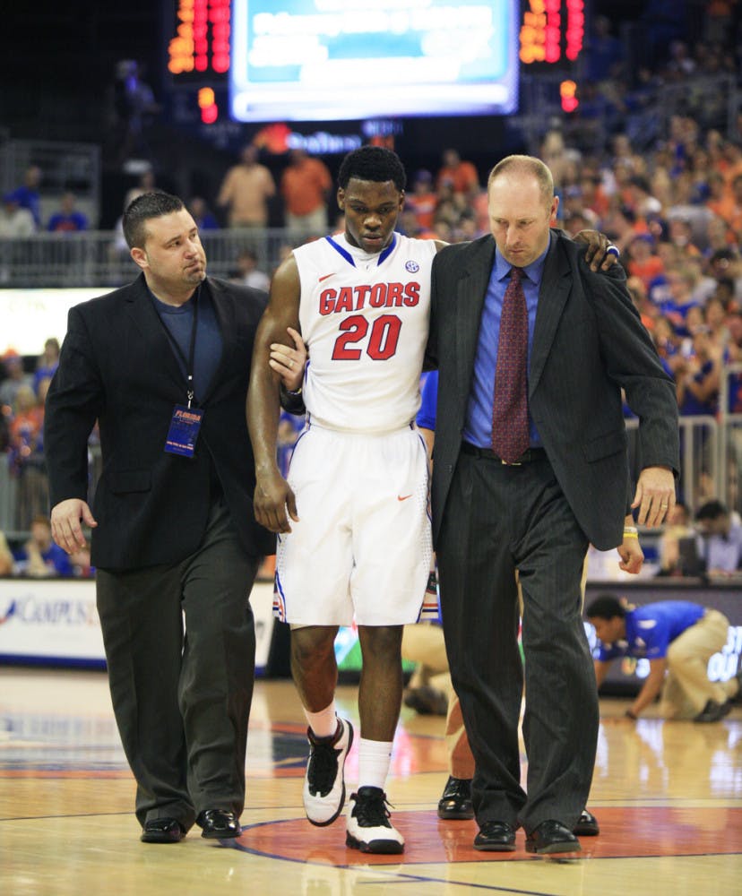 Trainers help Michael Frazier II (20) off the court after the freshman guard suffered a concussion in UF’s win against Arkansas on Saturday.
