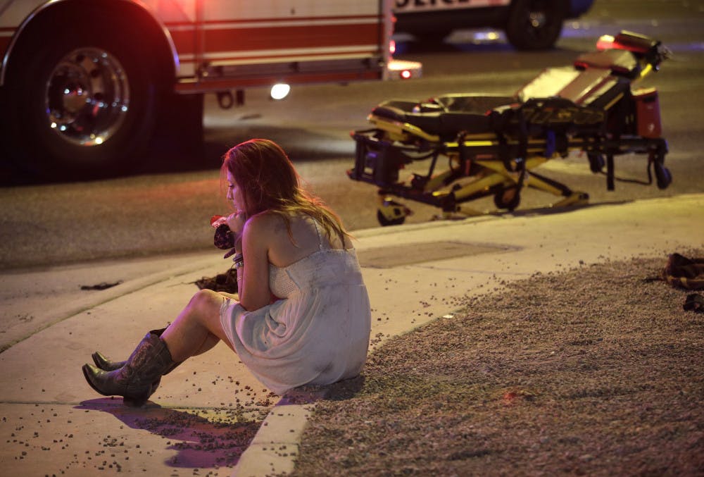 A woman sits on a curb at the scene of a shooting outside of a music festival along the Las Vegas Strip, Monday, Oct. 2, 2017, in Las Vegas. Multiple victims were being transported to hospitals after a shooting late Sunday at a music festival on the Las Vegas Strip.