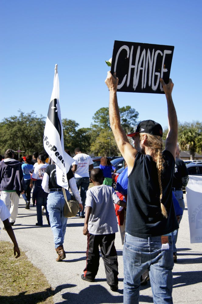 Coral MacDonald, a 50-year-old gardener, marches with his sign held high during the King Celebration Annual Commemorative March on Monday for Martin Luther King Jr. Day. A few steps ahead of him is Christine Wilson, a 66-year-old retired children's librarian, carrying a flag representing Veterans For Peace.