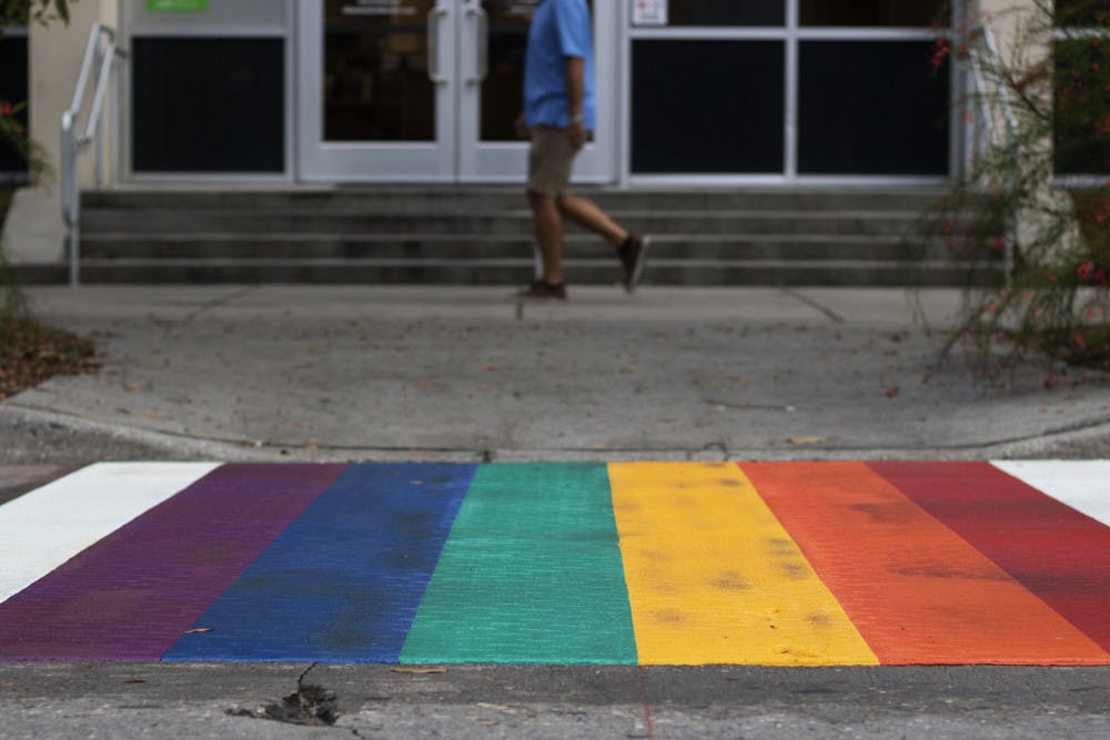 A pedestrian walks past one of the rainbow crosswalks Tuesday evening in downtown Gainesville near Bo Diddley Plaza.