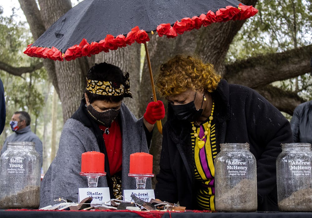 Gail K. Watson (left) and Brenda Whitfield (right) scoop dirt into glass jars at the soil ceremony for the Newberry Six on Friday, Feb. 5, 2021. Whitfield spoke during the ceremony before the crowd began adding earth to the containers.