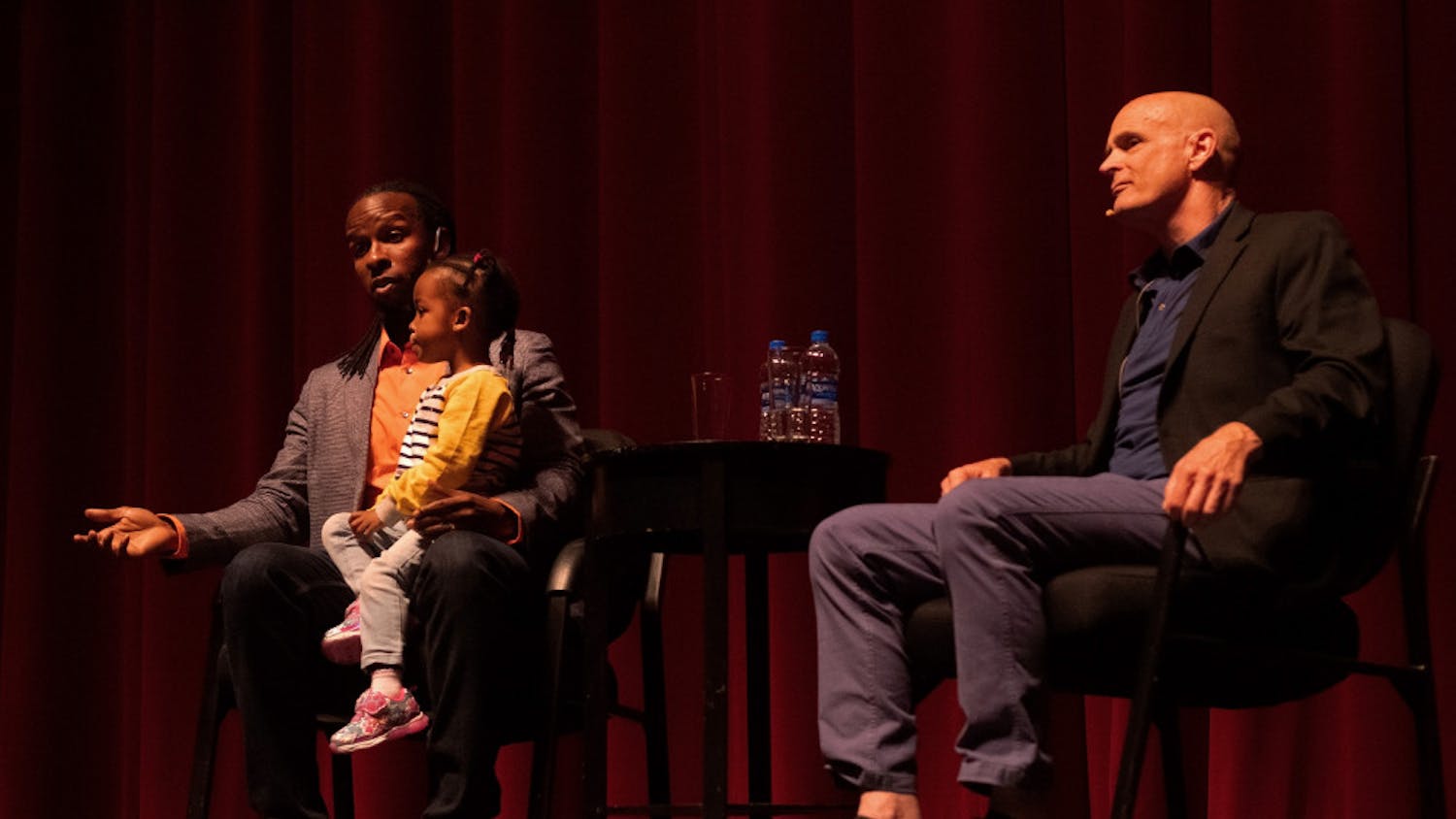Ibram X. Kendi answers an audience question during a question and answer session moderated by author and history professor Jack Davis while Kendi’s daughter sits in his lap at the Phillips Center for the Performing Arts Thursday night. About 1,230 people attended the event.
