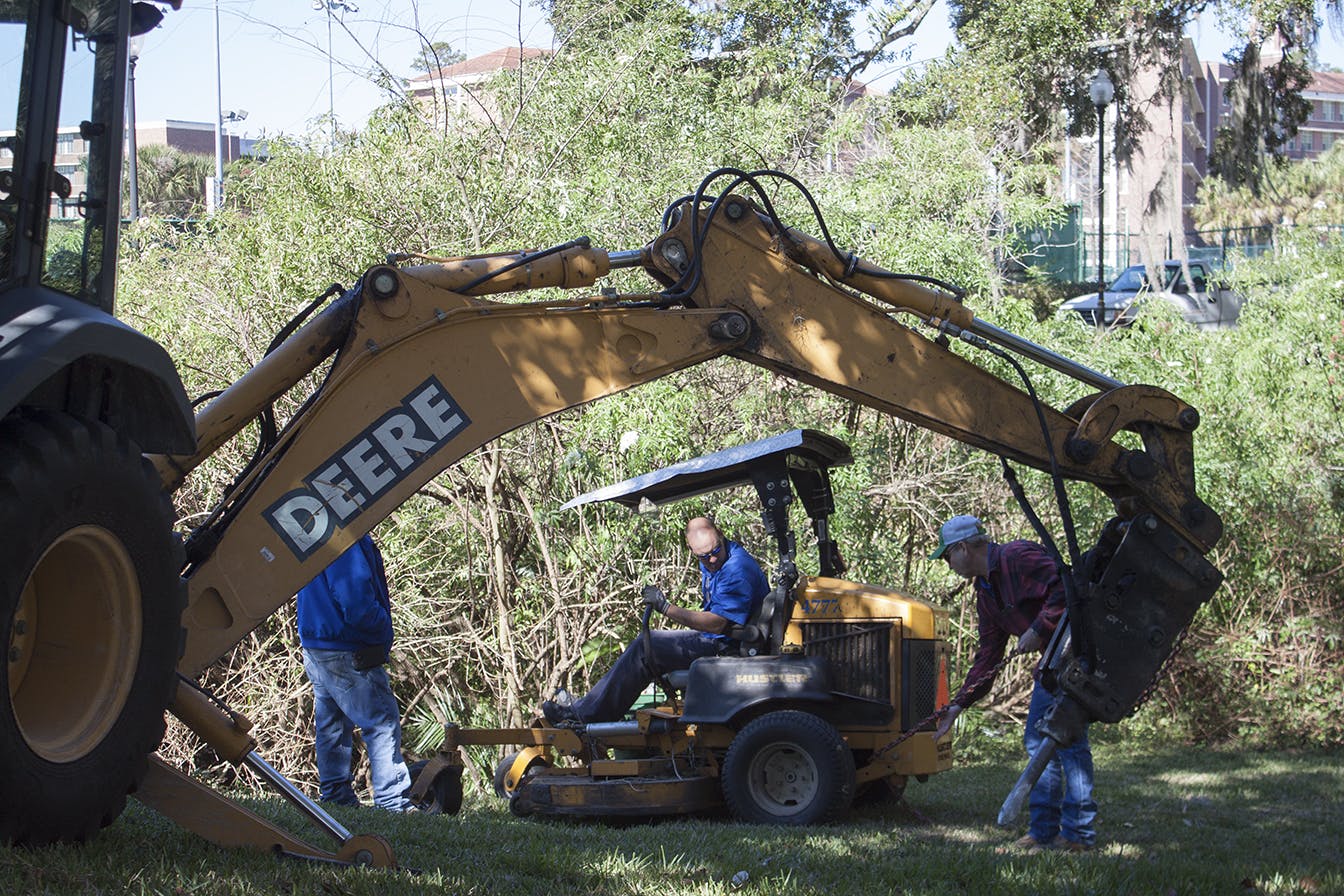A crew from the UF Physical Plant Division pulls a lawnmower out of a ditch after a worker fell into the ditch and injured his leg while mowing grass by Museum Road on Tuesday. Physical Plant Division workers watching the lawnmower get pulled from the ditch said they know and work with the man who was injured.