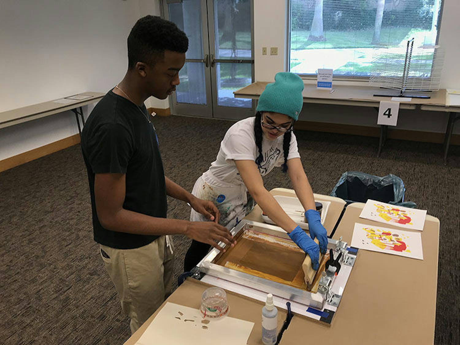 Reginald Carrol, 16, is instructed on the printmaking process by Harn volunteer Juana Diaz, 20. Diaz is a printmaking major at UF, and Carroll, who also performed a poem at the event, is a sophomore printmat Eastside High School.