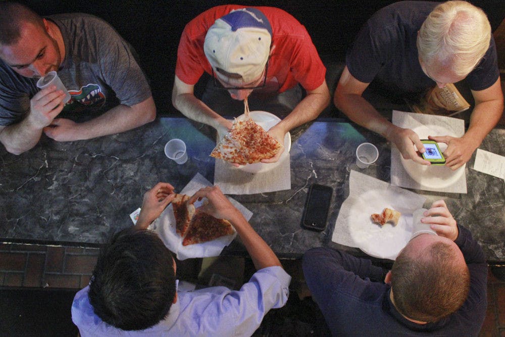 Alex Landry (top center), a 23-year-old UF alum, chews cheesy pizza with his group of friends who call themselves “The Gumby Guys” at Gumby’s Pizza’s 30th anniversary on Oct. 26, 2015. The group has been meeting at Gumby’s every Wednesday after Bible study for about 7 years. On Wednesday’s, Gumby’s has $0.50 pizza rolls. “For college kids,” Landry said, “it’s the dream.”