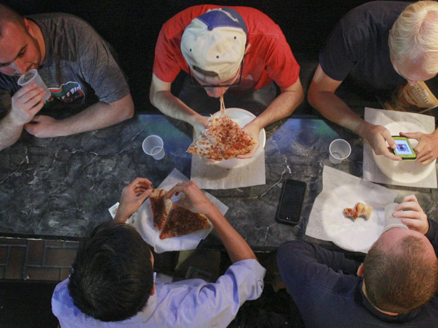Alex Landry (top center), a 23-year-old UF alum, chews cheesy pizza with his group of friends who call themselves “The Gumby Guys” at Gumby’s Pizza’s 30th anniversary on Oct. 26, 2015. The group has been meeting at Gumby’s every Wednesday after Bible study for about 7 years. On Wednesday’s, Gumby’s has $0.50 pizza rolls. “For college kids,” Landry said, “it’s the dream.”