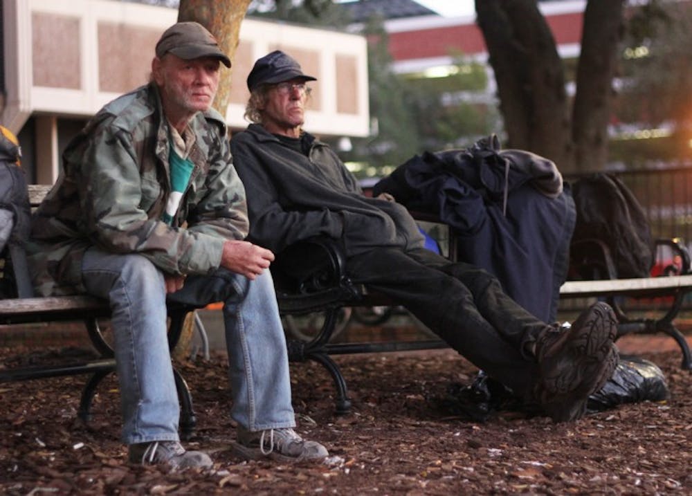 <p>John Roberts, 56, left, and Daniel Walters, 53, sit on a bench on Bo Diddley Community Plaza on Friday night. Temperatures will dip into the low 40s over the next few nights.</p>