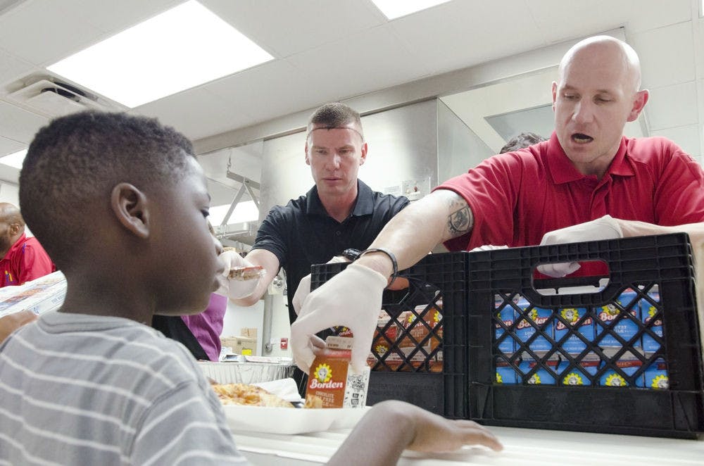 [FILE PHOTO] John Nordman, right, hands 8-year-old Micah Reed a chocolate milk at the Reichert House on Tuesday. Nine newly hired police officers served 128 students lunch.