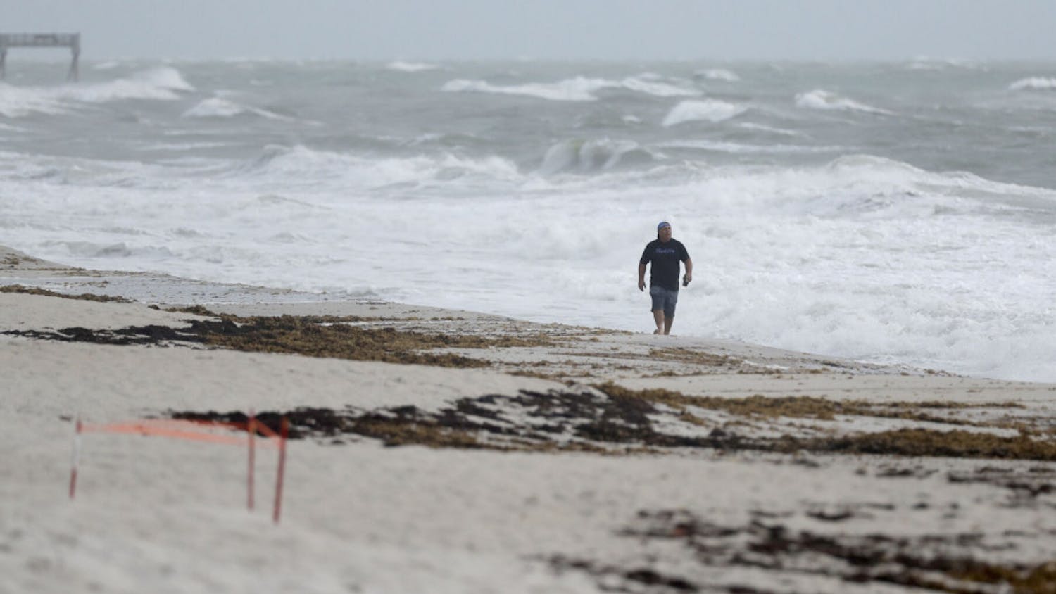 A beach goer walks along the shore as waves churned up by Tropical Storm Isaias crash near Jaycee Beach Park, Sunday, Aug. 2, 2020, in Vero Beach, Fla. Isaias weakened from a hurricane to a tropical storm late Saturday afternoon, but was still expected to bring heavy rain and flooding as it barrels toward Florida. (AP Photo/Wilfredo Lee)