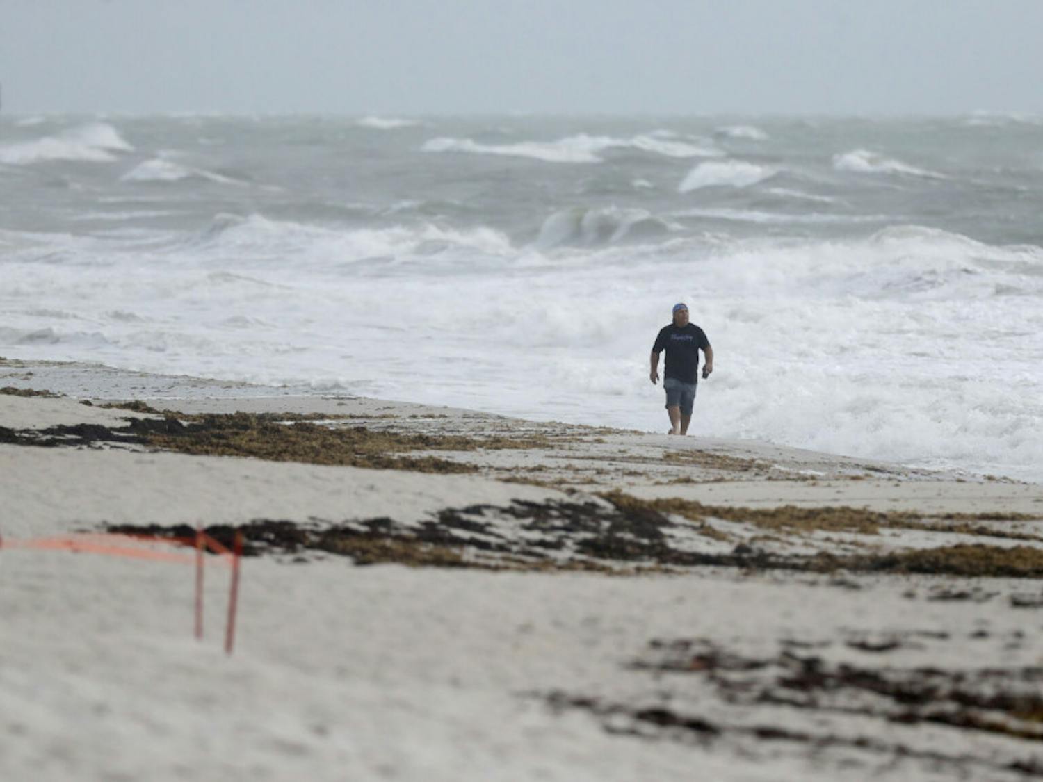 A beach goer walks along the shore as waves churned up by Tropical Storm Isaias crash near Jaycee Beach Park, Sunday, Aug. 2, 2020, in Vero Beach, Fla. Isaias weakened from a hurricane to a tropical storm late Saturday afternoon, but was still expected to bring heavy rain and flooding as it barrels toward Florida. (AP Photo/Wilfredo Lee)