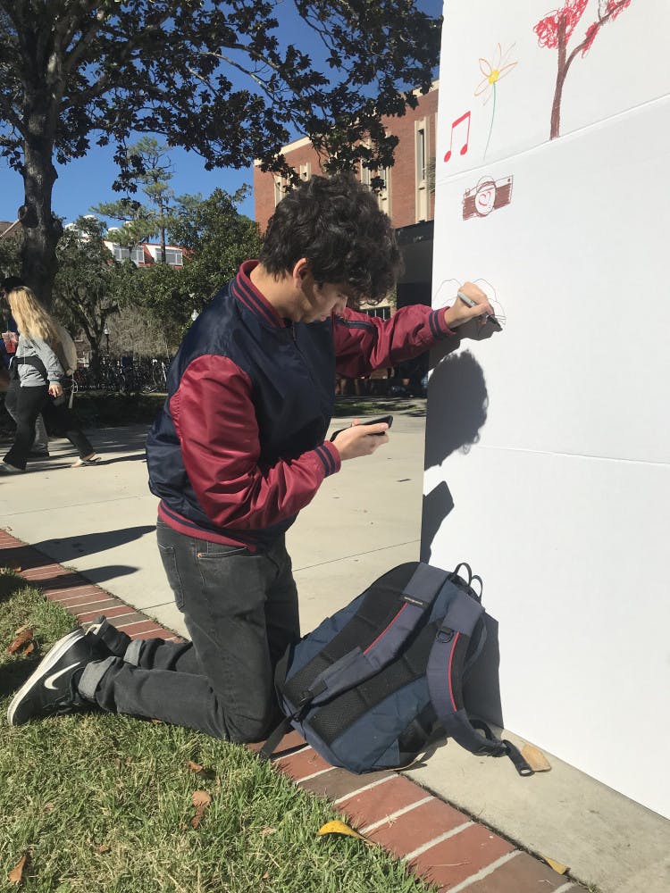 Lev Ettinger, 18, computer science freshman, looks at his phone for reference as he draws popular online meme Pepe the Frog on the “I Am More” wall. 