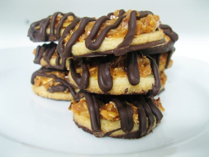 Samoas are simple shortbread cookies with a hole in the center, covered in a caramel and toasted coconut topping and then dipped in and streaked with rich dark chocolate.