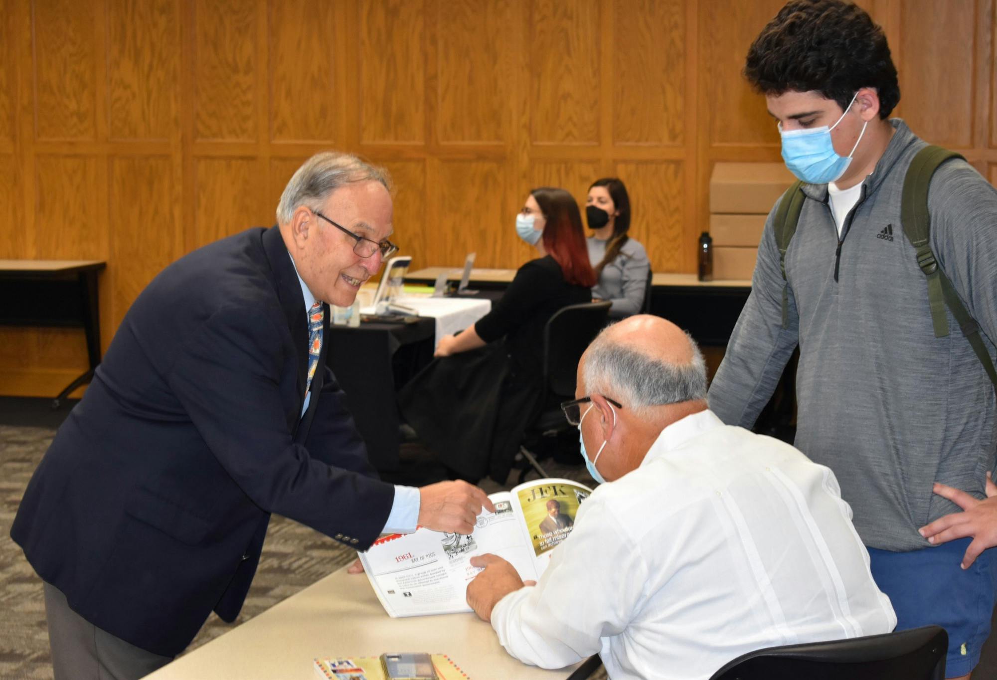 Emilio Cueto (left) points out a stamp in his book to his longtime friend Rafael Peñalver (center) on Monday, Nov. 15, 2021.