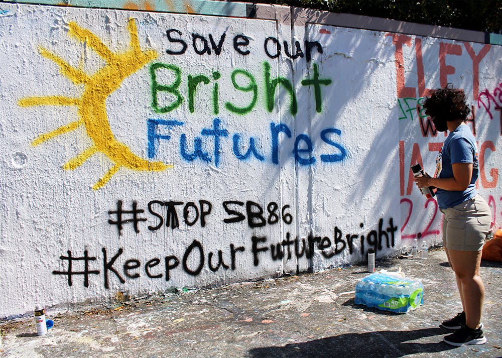 Alondra Arce, 20, a sustainability sophomore, looks at the “Save Our Bright Futures” mural she helped paint on the side of 34th Street in Gainesville on Sunday, March 7, 2021.