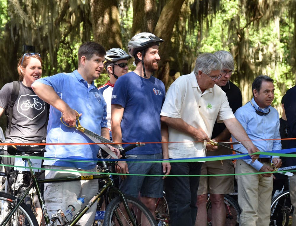 <p>Mayor Lauren Poe (left) and Alachua County Commissioner Hutch Hutchinson (right) cut the ribbons before the celebratory bike ride for the new UF Campus Greenway.</p>
