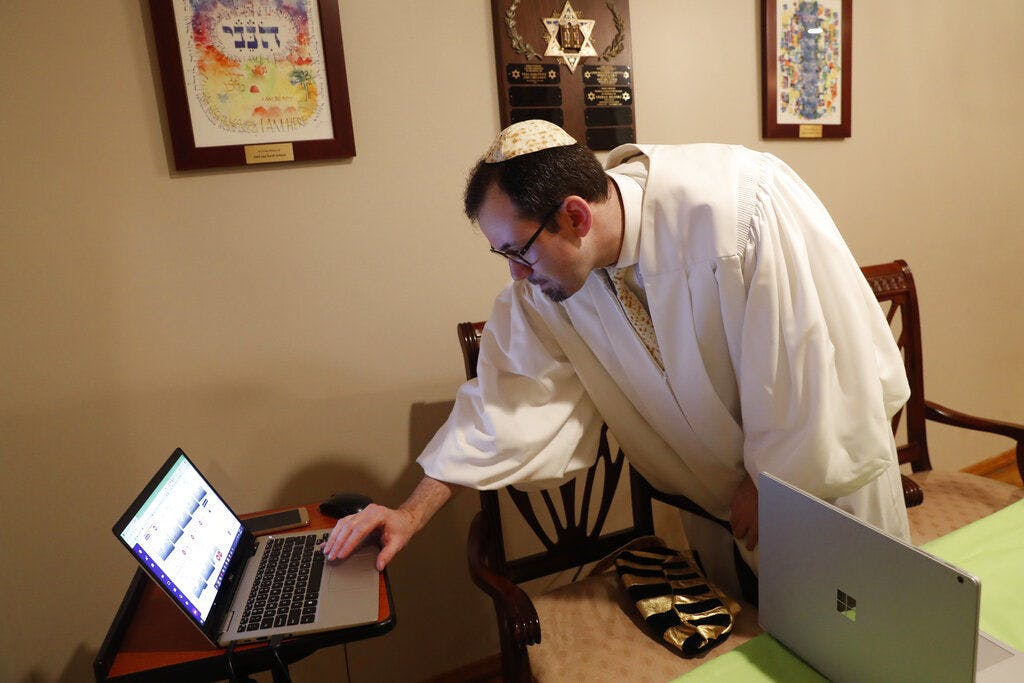 Rabbi Shlomo Segal of Kehilat Moshe synagogue checks to see who has dialed in to his virtual Passover seder in the Sheepshead Bay section of Brooklyn during the current coronavirus outbreak, Wednesday, April 8, 2020, in New York. Segal said some 55 congregants, friends and family members dialed into the tele-conferenced experience, which was also simulataneously broadcast live on YouTube on the other laptop, right. The new coronavirus causes mild or moderate symptoms for most people, but for some, especially older adults and people with existing health problems, it can cause more severe illness or death. (AP Photo/Kathy Willens)