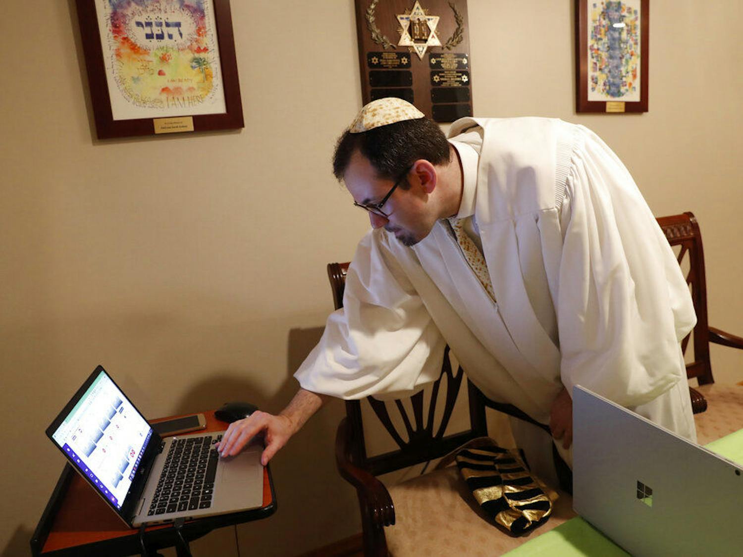 Rabbi Shlomo Segal of Kehilat Moshe synagogue checks to see who has dialed in to his virtual Passover seder in the Sheepshead Bay section of Brooklyn during the current coronavirus outbreak, Wednesday, April 8, 2020, in New York. Segal said some 55 congregants, friends and family members dialed into the tele-conferenced experience, which was also simulataneously broadcast live on YouTube on the other laptop, right. The new coronavirus causes mild or moderate symptoms for most people, but for some, especially older adults and people with existing health problems, it can cause more severe illness or death. (AP Photo/Kathy Willens)